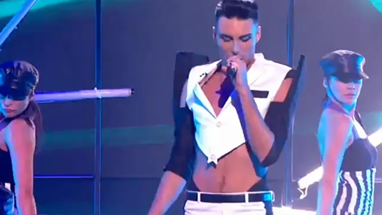 Rylan Clark on stage in singing in 2012 with two women dancing with him - cloths in black and white.