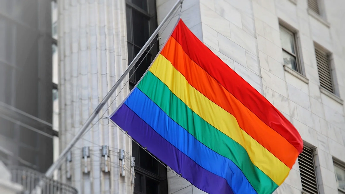 A LGBTQ flag flying in front of a building